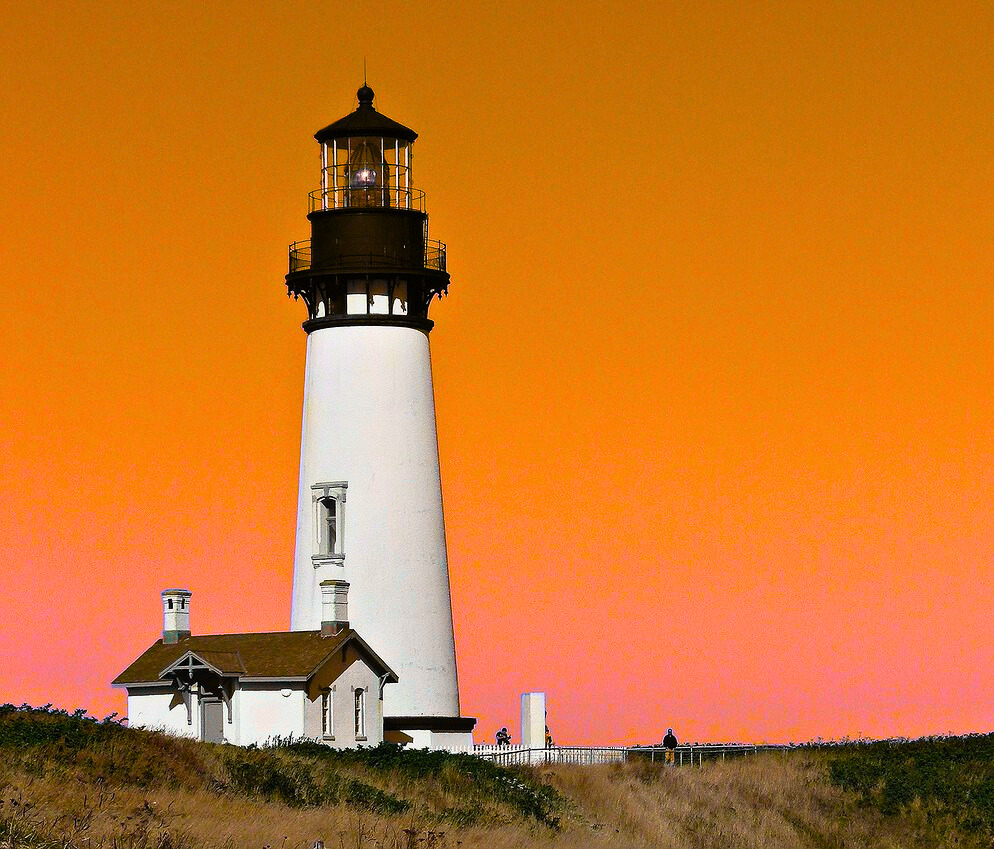 White lighthouse on the Oregon coast against an orange and pink sky