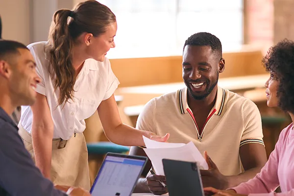 Colleagues laughing around laptops at a shared table