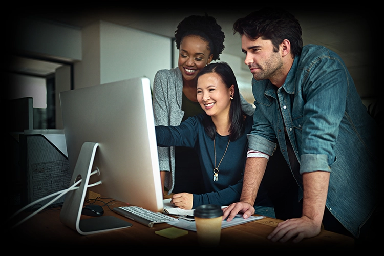 Three colleagues smiling at a desktop monitor