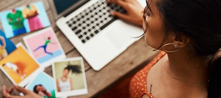 Hands typing on a laptop beside printed photos, seen from above