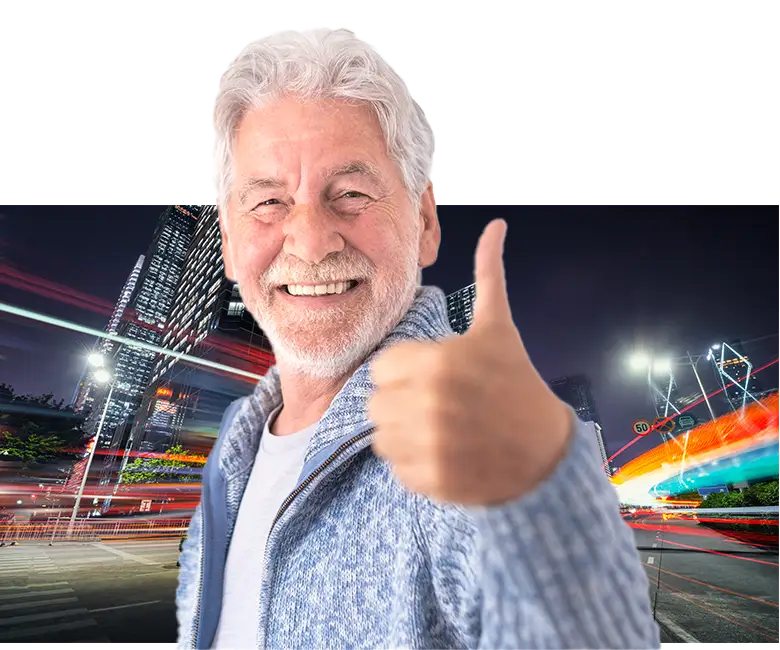 Older man giving a thumbs up in front of city light trails